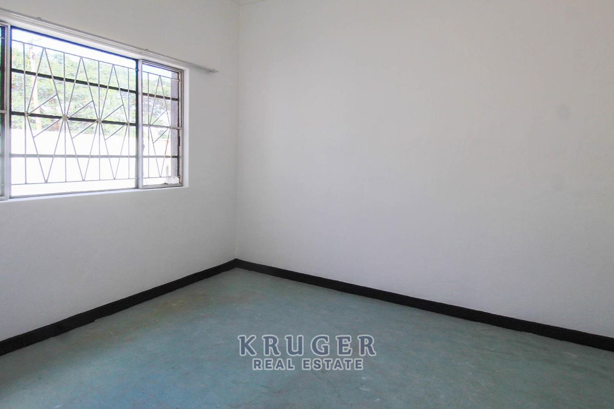 A vacant bedroom featuring plain white walls, simple flooring, and a window fitted with security bars.