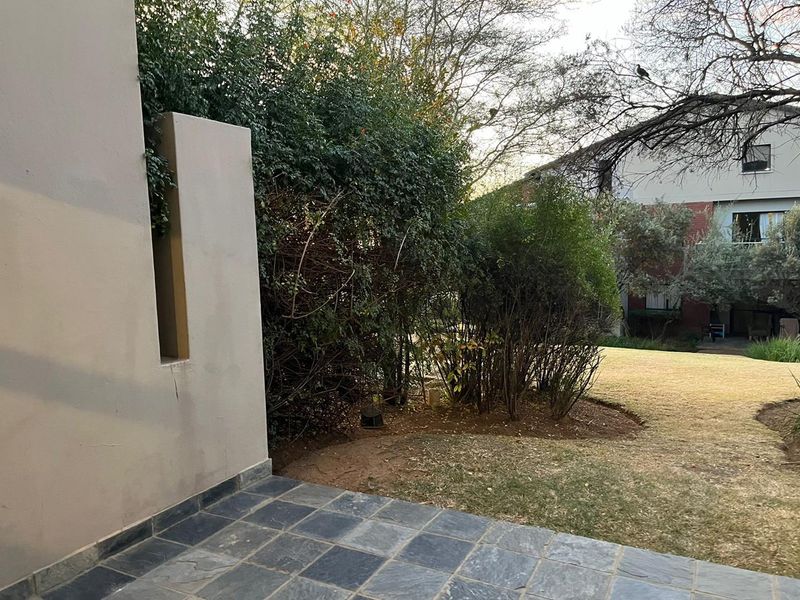 A private rear patio area featuring dark stone tiling, overlooking a shared garden space with established greenery.