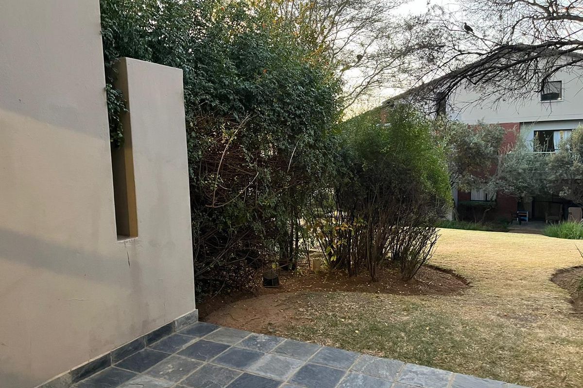 A private rear patio area featuring dark stone tiling, overlooking a shared garden space with established greenery.
