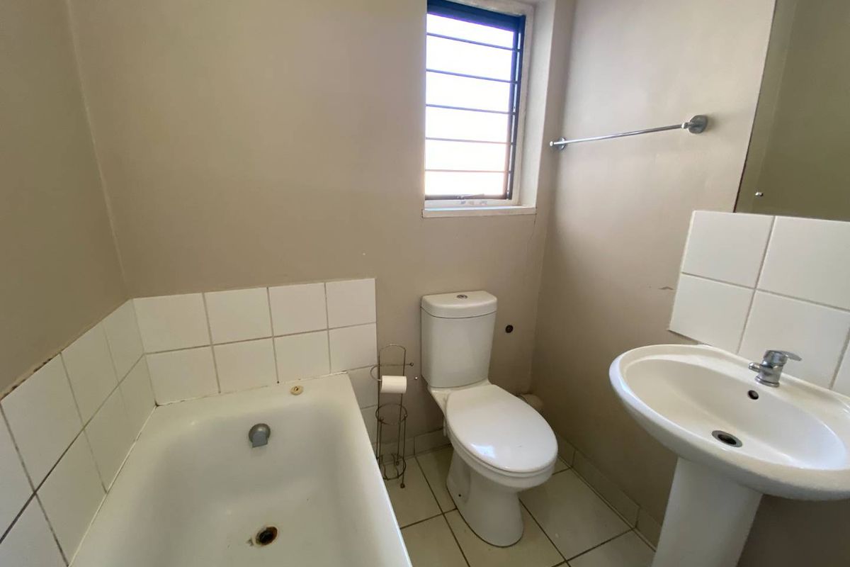 A functional bathroom featuring a standard bathtub, pedestal basin, and toilet, with tiled flooring and a window for natural light.