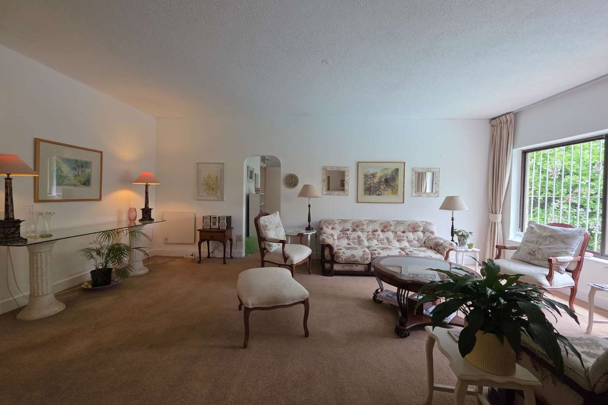 Spacious living room featuring neutral walls, carpeted flooring, and a large window with security bars, offering a comfortable and traditional living space.