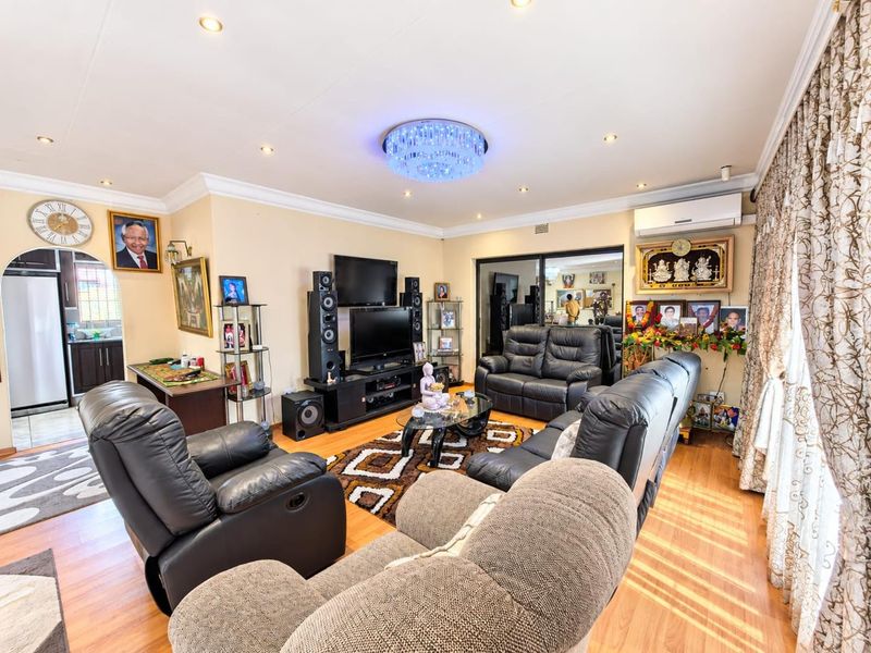 A well-maintained living room featuring laminate flooring, recessed downlighting, a decorative crystal chandelier, and a wall-mounted split-system air conditioner.
