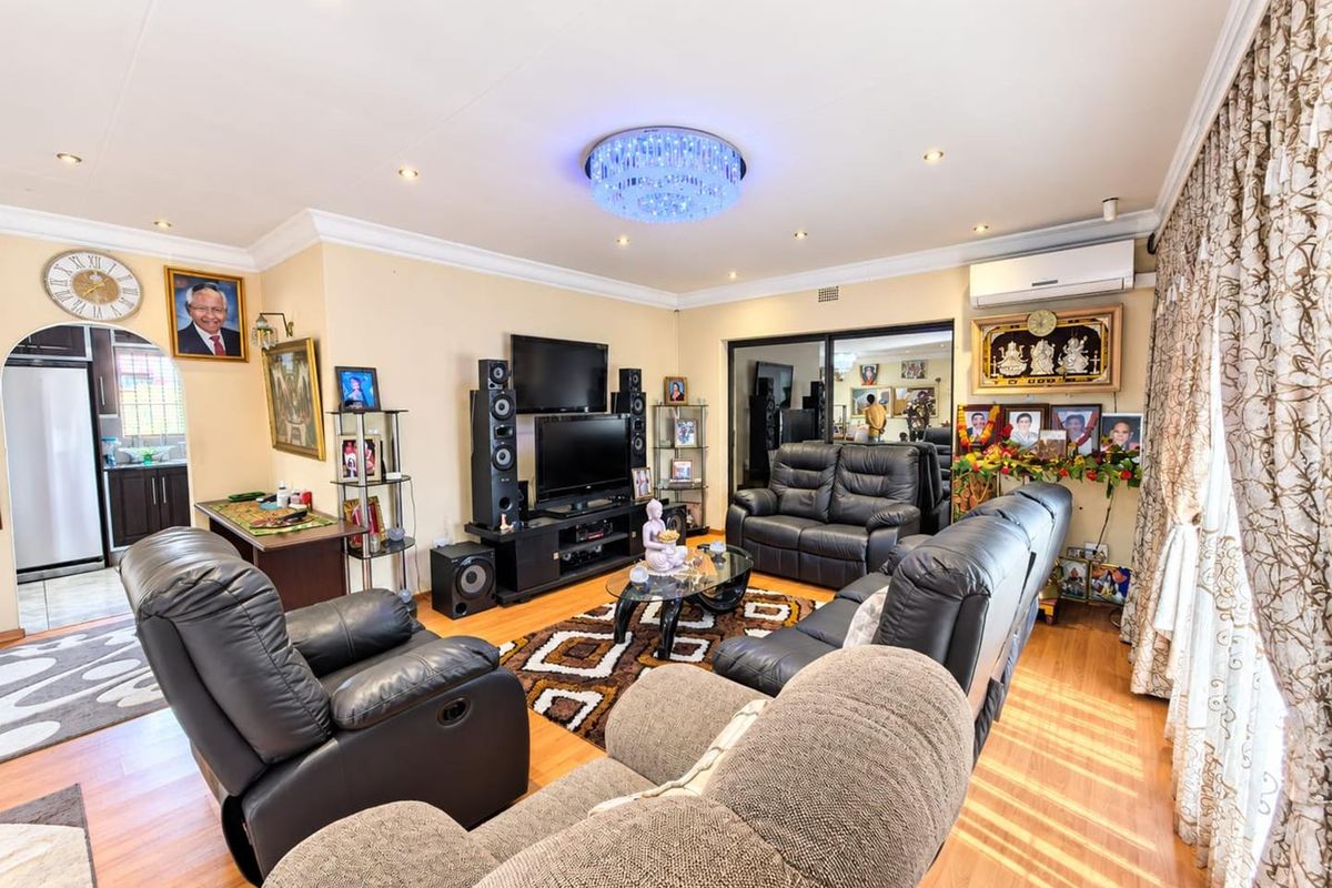 A well-maintained living room featuring laminate flooring, recessed downlighting, a decorative crystal chandelier, and a wall-mounted split-system air conditioner.