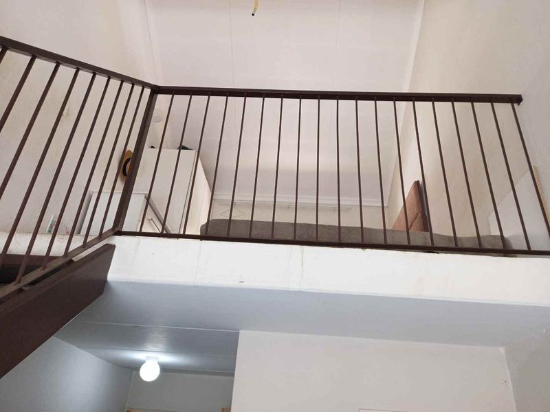 A mezzanine bedroom level featuring a metal safety balustrade, overlooking the lower living area.