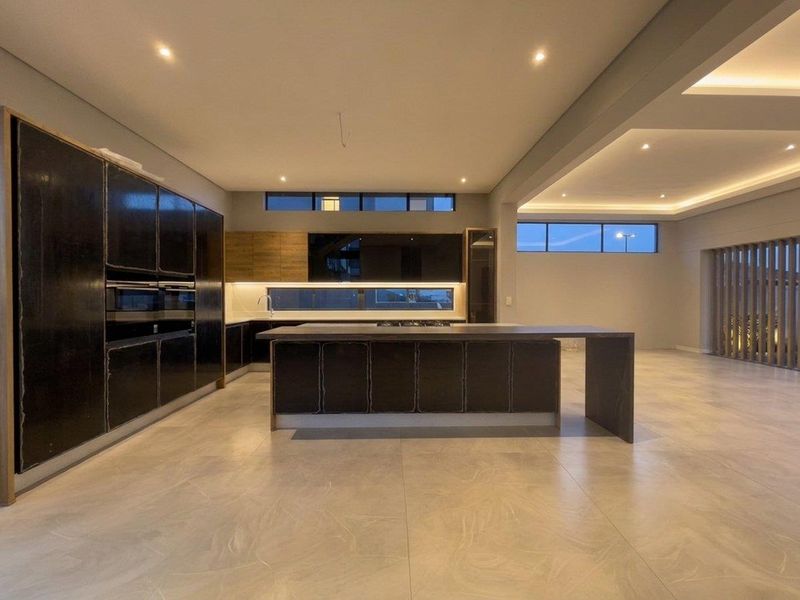 Modern open-plan kitchen featuring a large central island, sleek dark cabinetry, integrated appliances, and recessed lighting in a spacious, contemporary living area.