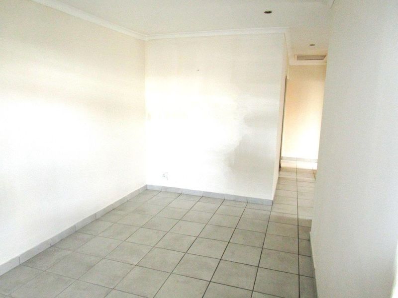 An empty, neutrally painted living area featuring tiled flooring and recessed downlights, offering a blank canvas for potential interior design updates.