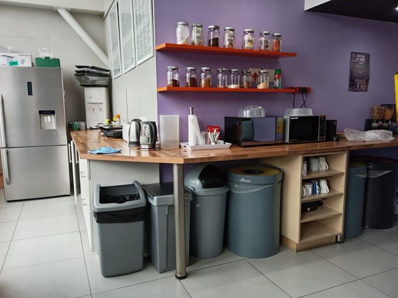 A functional office kitchen area featuring wooden countertops, floating storage shelves, and tiled flooring, providing a practical space for staff refreshments.
