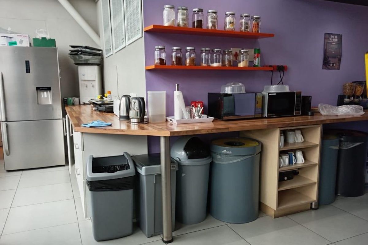 A functional office kitchen area featuring wooden countertops, floating storage shelves, and tiled flooring, providing a practical space for staff refreshments.