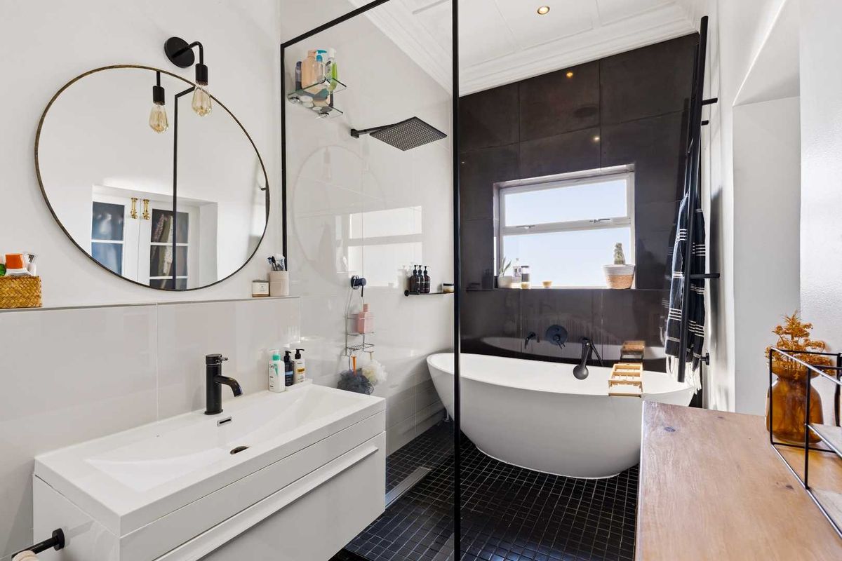 Modern bathroom featuring a sleek freestanding bathtub, glass-enclosed rain shower, wall-mounted vanity, and contemporary black fixtures with high-quality finishes.