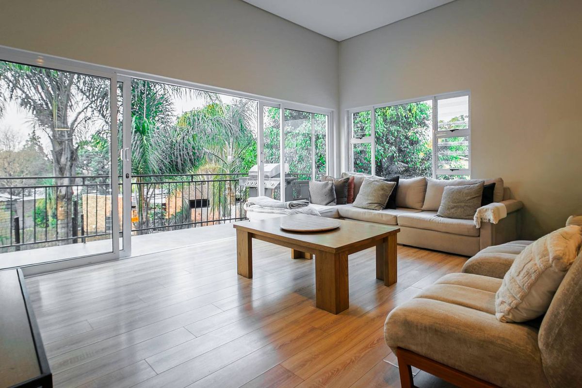 Spacious living room featuring laminate flooring and large sliding glass doors that open onto a balcony with lush garden views.