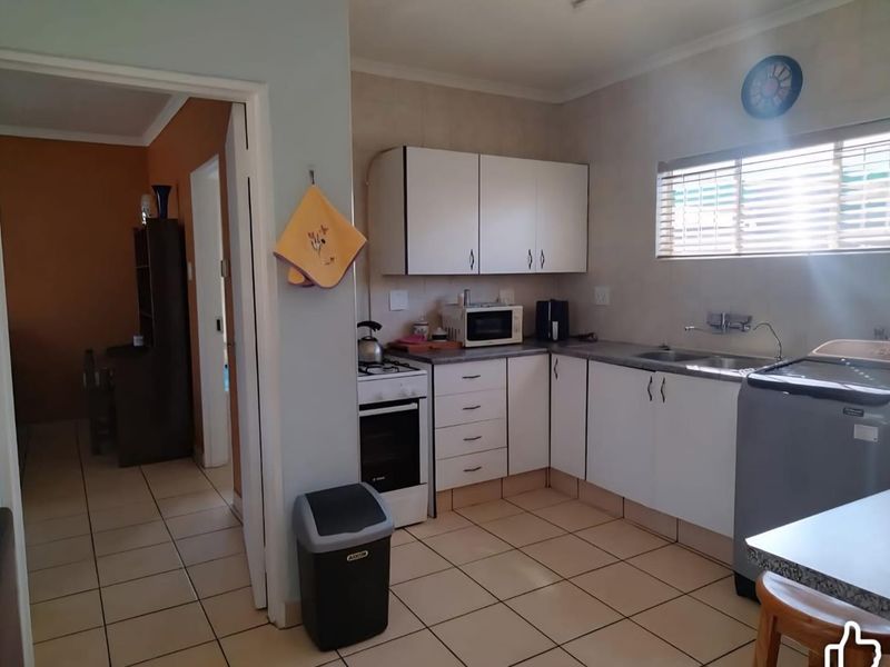 Functional kitchen featuring white cabinetry, laminate countertops, a stainless steel double sink, and tiled flooring, with an adjacent doorway leading to another room.