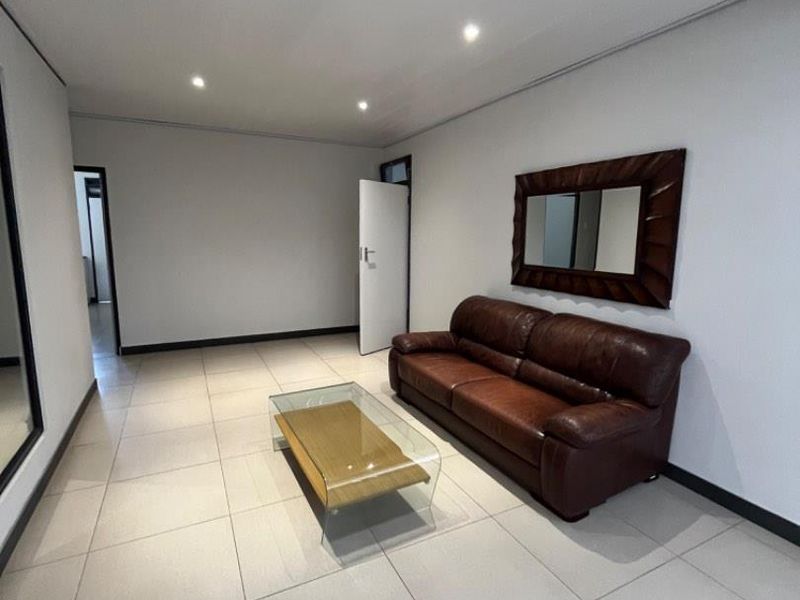 A bright, open-plan living area featuring neutral floor tiles, recessed ceiling lighting, and clean white walls, providing a versatile space for business use.