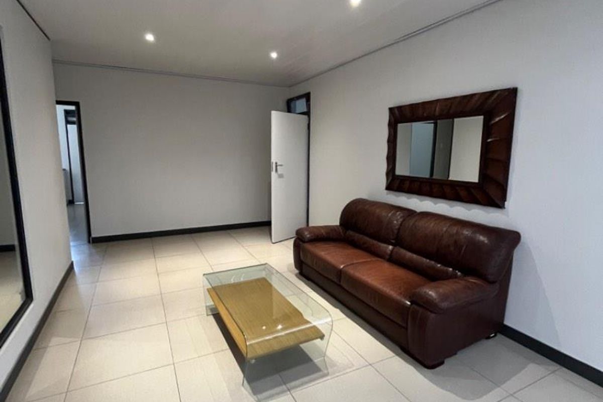 A bright, open-plan living area featuring neutral floor tiles, recessed ceiling lighting, and clean white walls, providing a versatile space for business use.