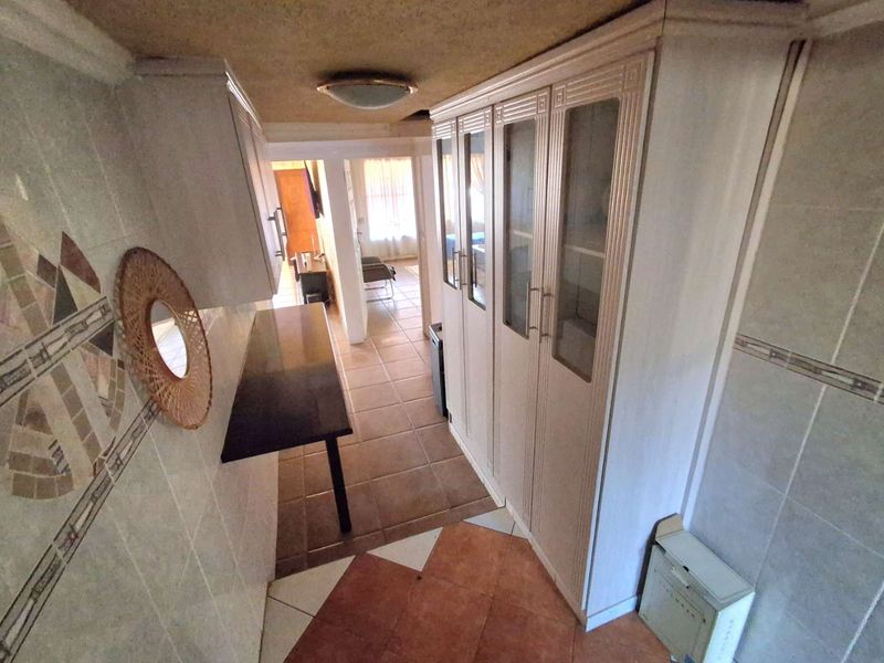 A functional scullery or utility area featuring built-in cabinetry, tiled walls, and floor tiles, offering potential for modernization and improved storage utility.