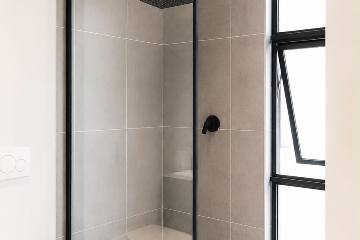 Modern bathroom featuring a walk-in shower with a black frame, rainfall showerhead, and neutral grey wall tiling.