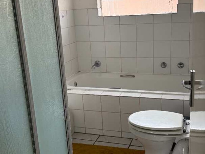 A functional bathroom featuring a built-in bathtub, separate shower enclosure, and tiled finishes. The space would benefit from cosmetic updates to modernize the fixtures.