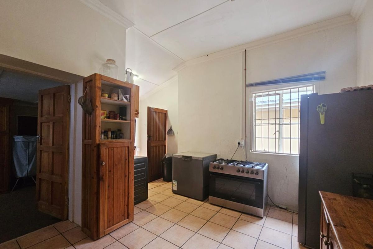A functional kitchen area featuring tiled flooring, a freestanding gas stove, and built-in wooden cabinetry with access to adjacent rooms.