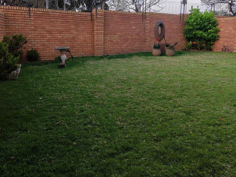 A private garden area featuring a well-maintained lawn enclosed by a high brick boundary wall with integrated razor wire security fencing.