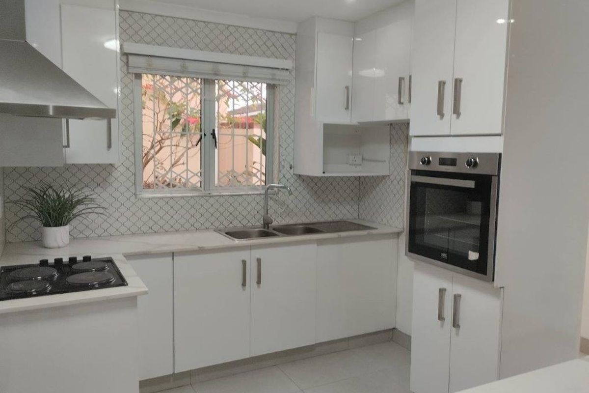 Modern kitchen featuring white gloss cabinetry, built-in oven, electric hob, stainless steel extractor fan, and a stylish tiled backsplash with a double bowl sink.