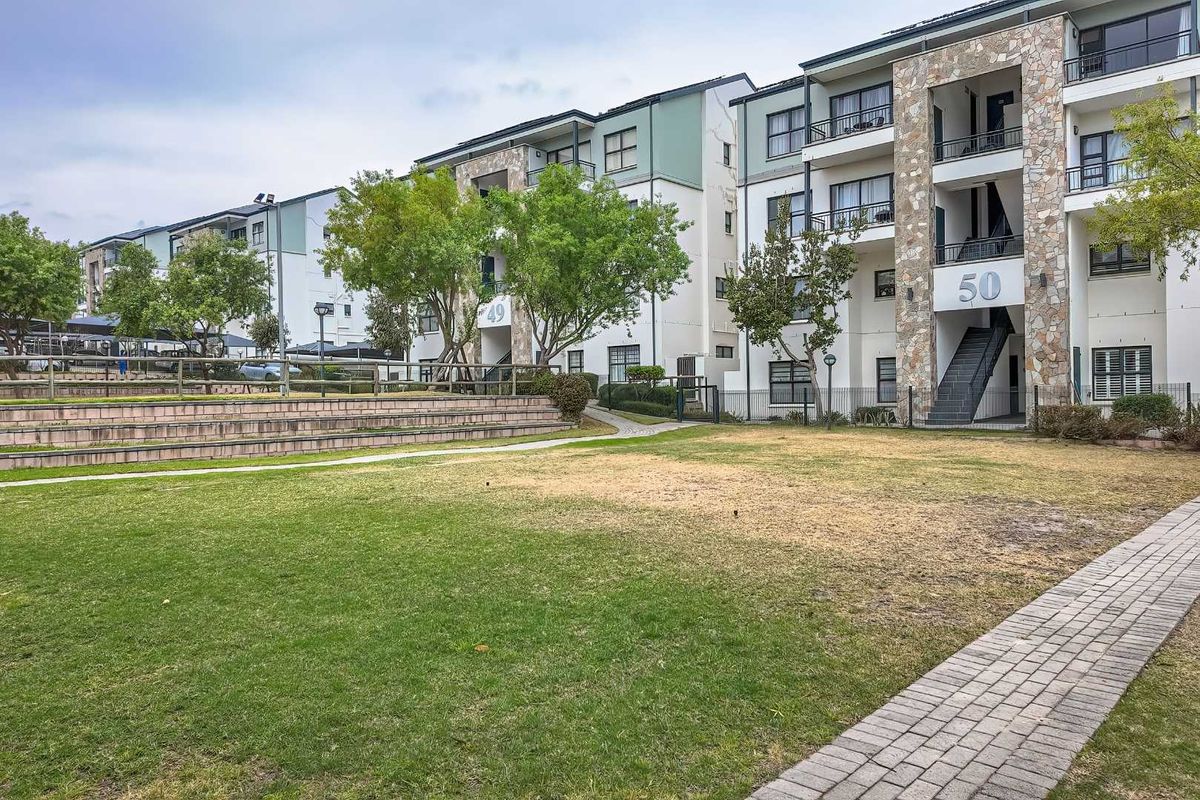 Exterior view of a multi-story apartment complex featuring stone-clad facades, private balconies, and a shared landscaped garden area with a paved walkway.