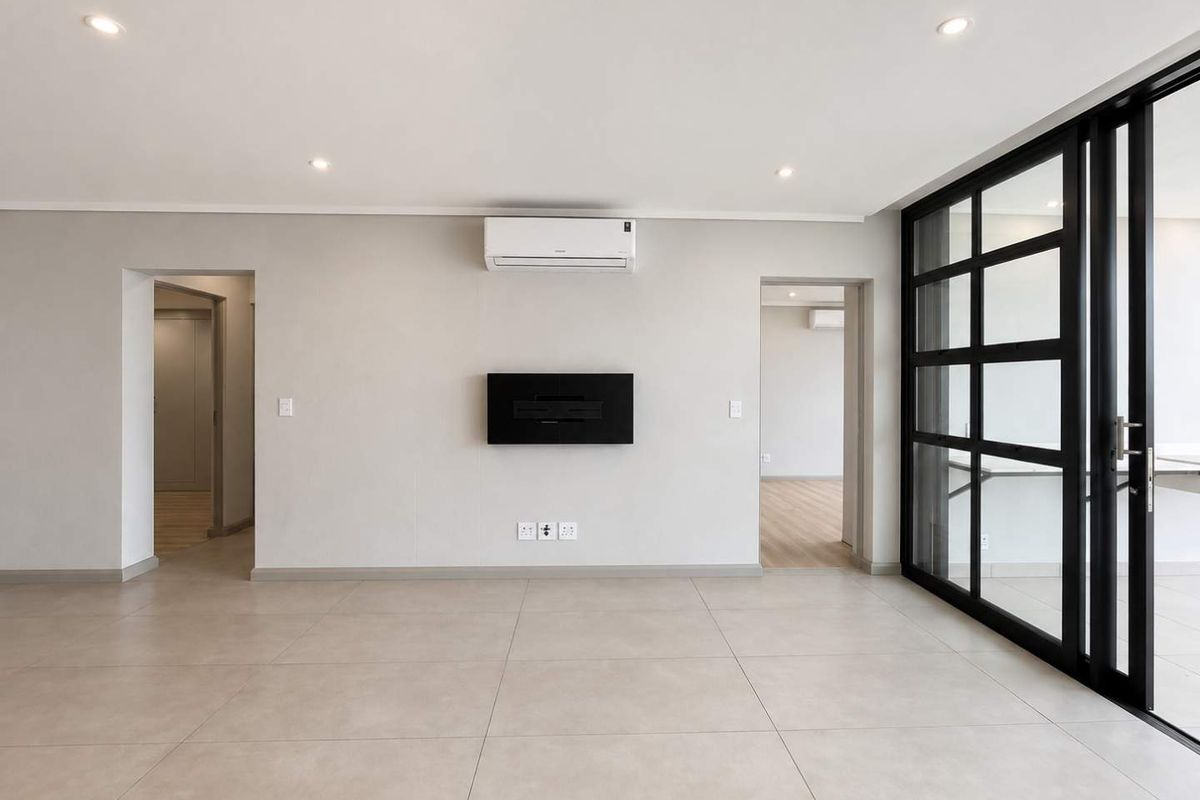 A bright, modern, and empty living area featuring large-format floor tiles, a wall-mounted electric fireplace, split-system air conditioning, and black-framed glass sliding doors.