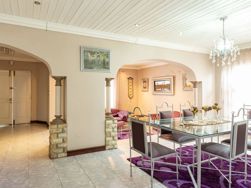 Spacious dining area featuring elegant archways, decorative stone-clad columns, tiled flooring, and a classic chandelier, creating a warm and inviting atmosphere.