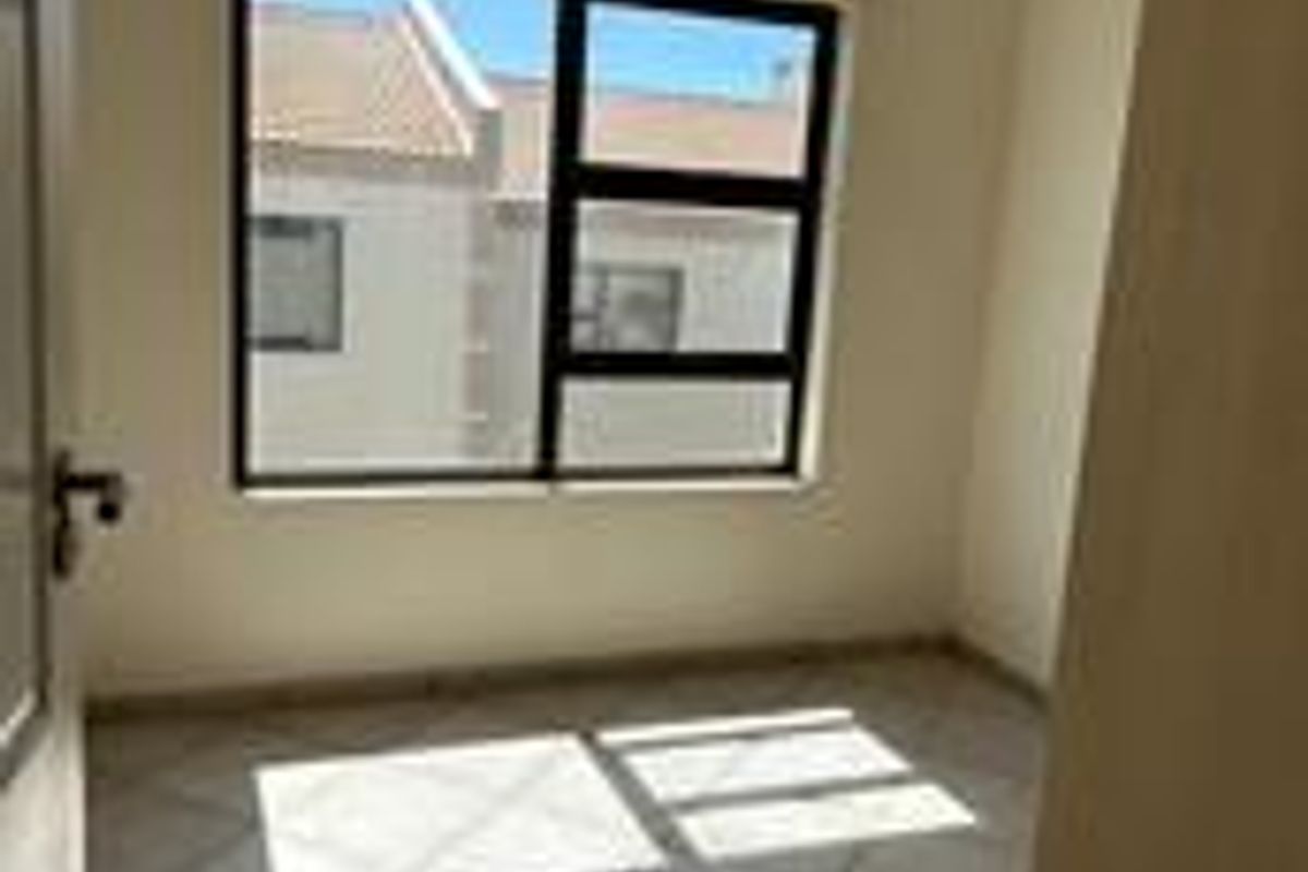A bright, empty bedroom featuring neutral tiled flooring and a large window with dark frames, offering a clean and versatile living space.