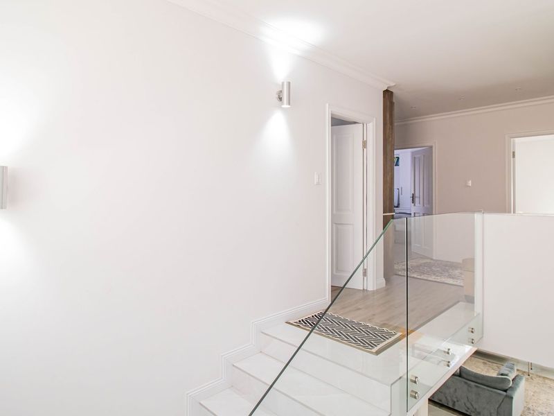 A bright and modern landing area featuring a glass balustrade, clean white walls, and contemporary wall-mounted lighting.