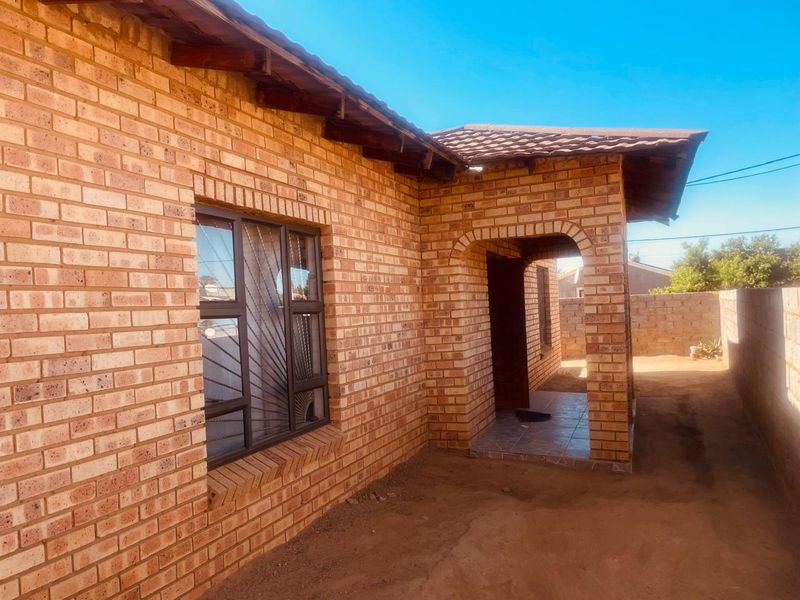 A view of the rear exterior of a face brick house featuring a covered porch area and a surrounding perimeter wall.