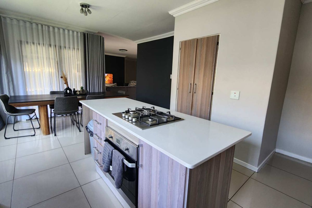 Modern open-plan kitchen featuring a central island with a built-in gas hob and oven, flowing seamlessly into the adjacent dining and living areas.