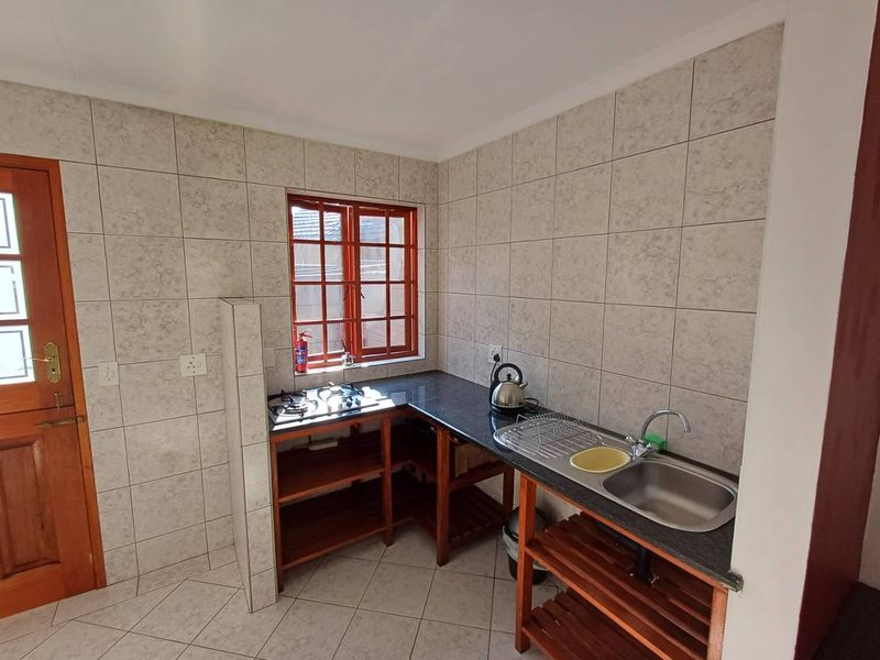 Compact kitchen featuring granite countertops, a gas hob, stainless steel sink, and full-height wall tiling with wooden joinery.