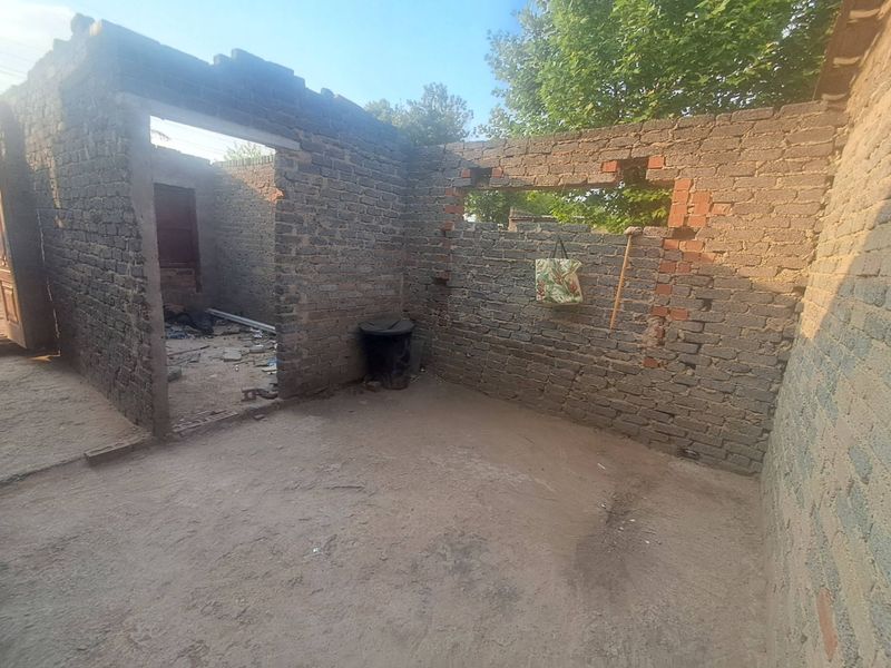 An exterior view of a property in a state of severe disrepair, featuring exposed brick walls and an unfinished structure with no roof.