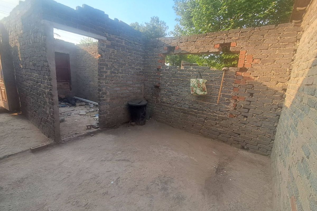An exterior view of a property in a state of severe disrepair, featuring exposed brick walls and an unfinished structure with no roof.