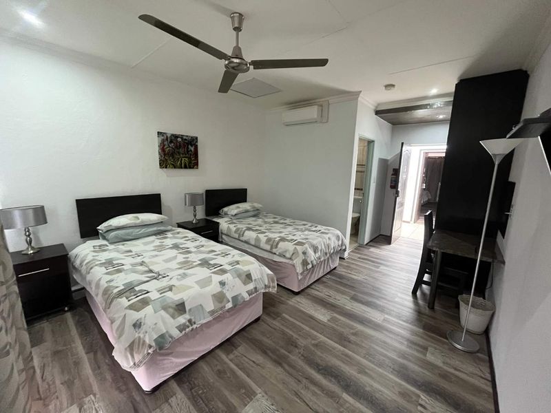 A well-maintained bedroom featuring laminate flooring, a ceiling fan, and a split-system air conditioner, with an adjoining en-suite bathroom.