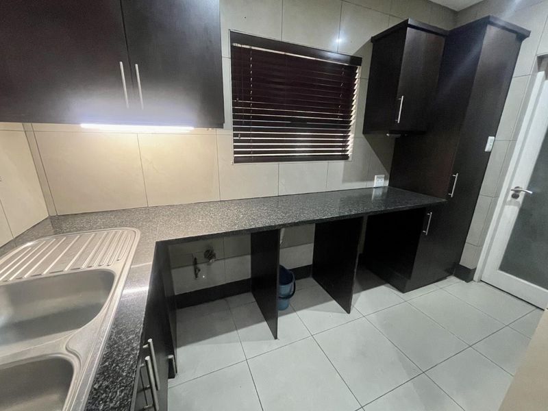 A clean, modern kitchen featuring dark wood cabinetry, granite countertops, a stainless steel double sink, and neutral tiled finishes.
