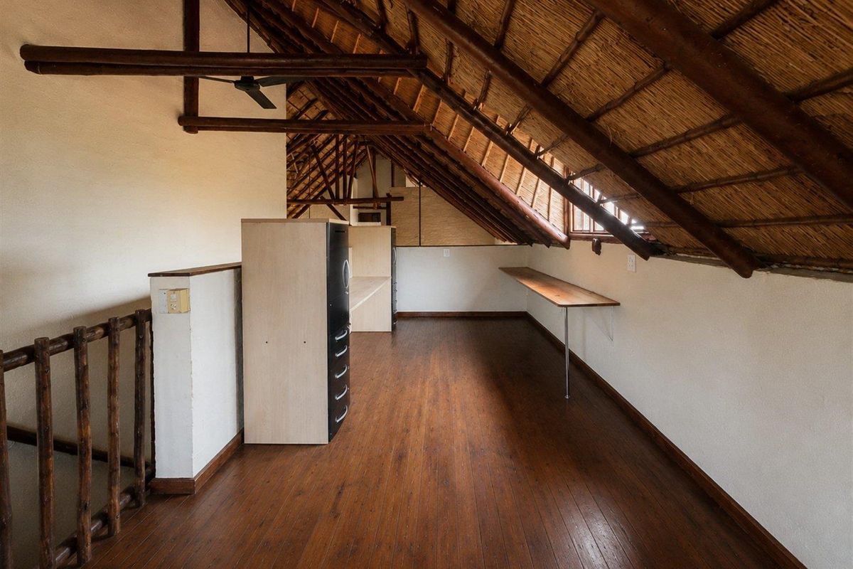 An attic-style loft space featuring exposed timber rafters, a traditional thatched roof, wooden flooring, and a built-in desk area.