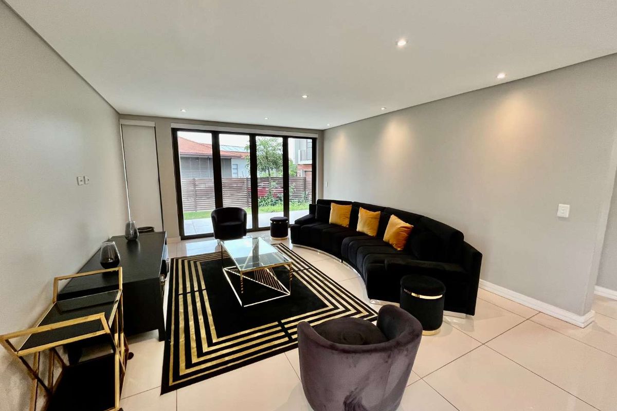 A modern, open-plan living area featuring large glass sliding doors that provide access to the rear garden, complemented by recessed ceiling lighting and tiled flooring.