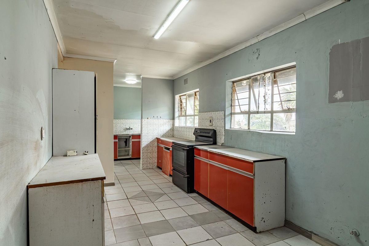 A dated kitchen featuring original cabinetry, tiled flooring, and a freestanding stove, requiring significant renovation and cosmetic updates to modernize the space.