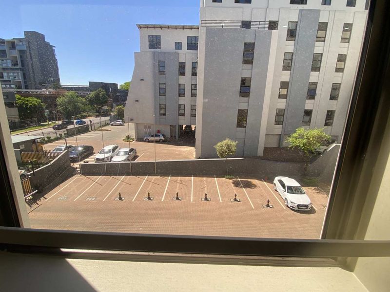 An elevated view from an apartment window overlooking a paved parking area and surrounding residential building complex.