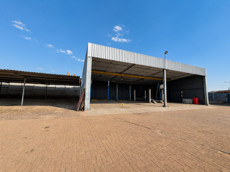 Spacious open-sided industrial garage featuring a paved forecourt, steel structural framing, and an integrated vehicle service lift, suitable for automotive or workshop use.