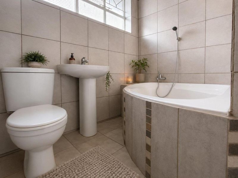 A well-maintained bathroom featuring a pedestal basin, toilet, and a built-in bathtub with a handheld shower mixer, finished with neutral wall and floor tiles.