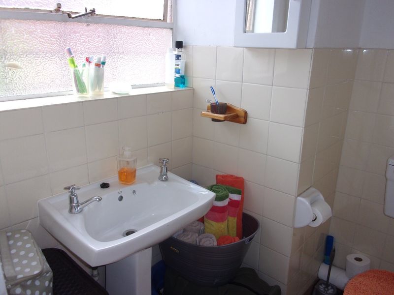 A functional bathroom featuring a pedestal basin, tiled walls, and a window, currently showing signs of age and wear in the finishes.