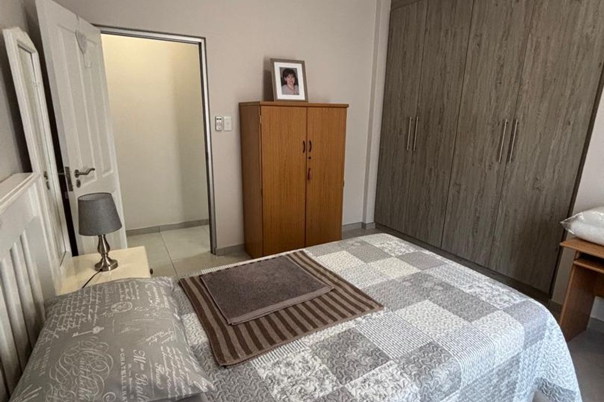 A well-maintained bedroom featuring built-in wooden cupboards, neutral wall finishes, and tiled flooring, providing a clean and functional living space.