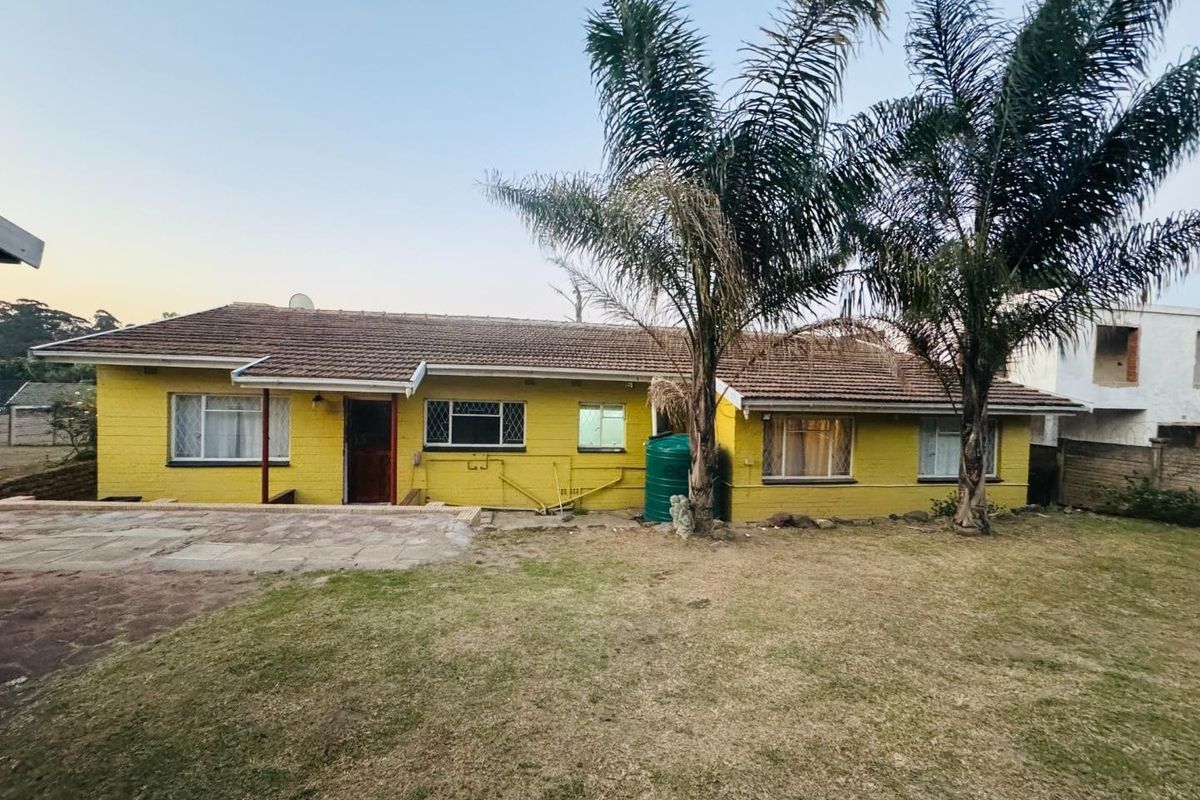Rear view of a single-story townhouse featuring a yellow brick facade, tiled roof, paved patio area, and a garden with mature palm trees.