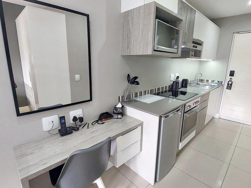 Modern compact kitchen featuring built-in cabinetry, integrated appliances including a hob and oven, and a convenient built-in desk area with tiled flooring.