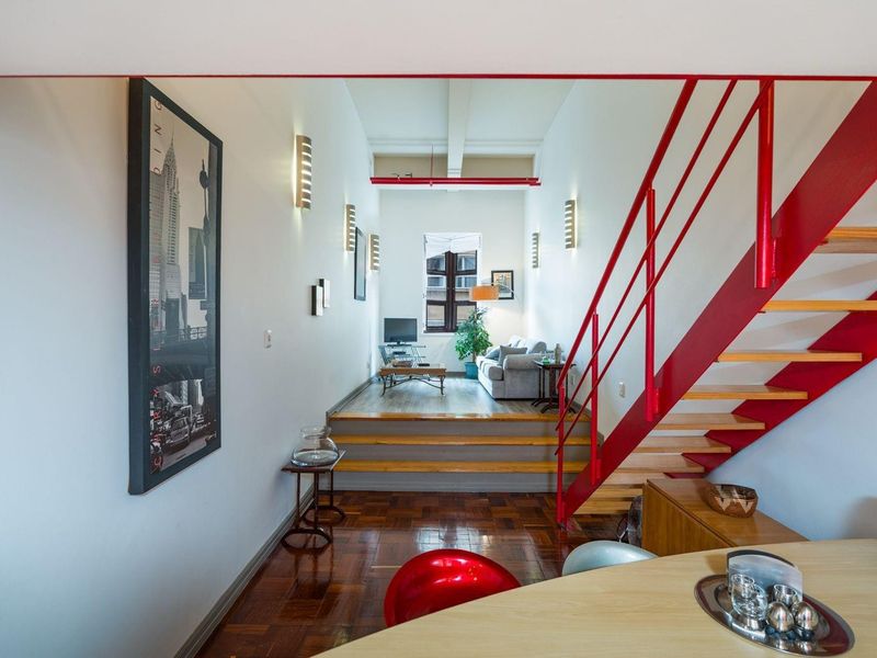 Open plan living area featuring a striking red staircase, parquet flooring, and a raised platform leading to a bright, naturally lit lounge space.