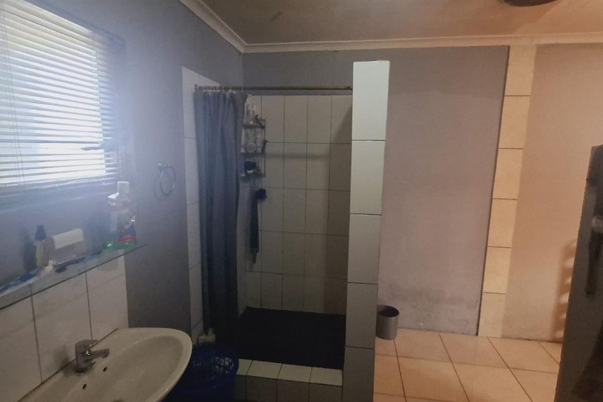 A functional bathroom featuring a pedestal basin, tiled shower enclosure, and tiled flooring, requiring cosmetic updates to improve its overall condition.
