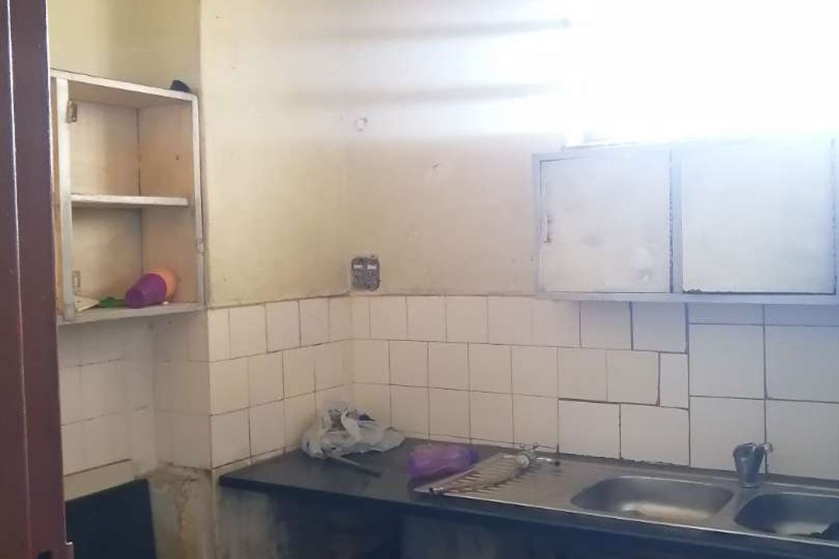 A dated kitchen area requiring significant renovation, featuring a basic sink, tiled splashback, and visible signs of ceiling water damage and structural wear.