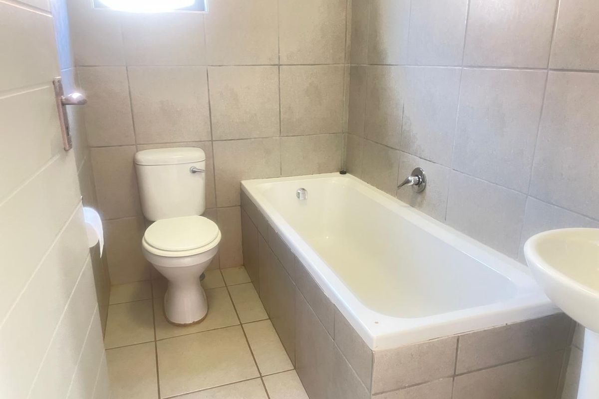 A functional bathroom featuring a standard bathtub, pedestal basin, and toilet with neutral wall and floor tiling.