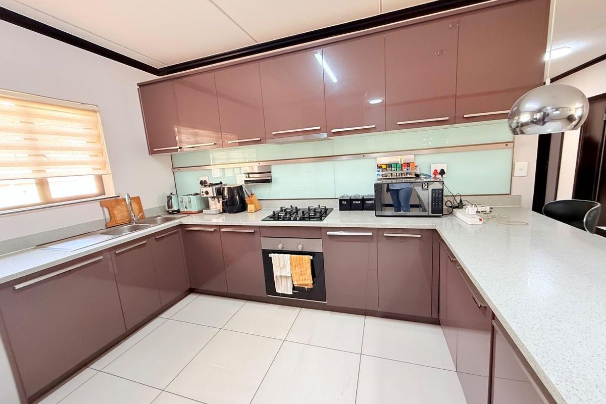 Modern kitchen featuring high-gloss cabinetry, stone countertops, a built-in oven, gas hob, and a glass splashback with tiled flooring.